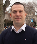 Smiling man with close-cropped short brown hair, wearing a black sweater with snow on ground in background